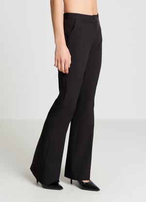 Pantalon évasé noir en tissu lisse, doté d'une fermeture par boutons, de poches avant et d'une taille ajustée, stylisé avec des talons noirs à bouts pointus.