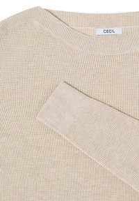 Pull en tricot beige avec col rond et poignets côtelés, présentant une texture tissée et une étiquette de marque visible à l'intérieur du col.