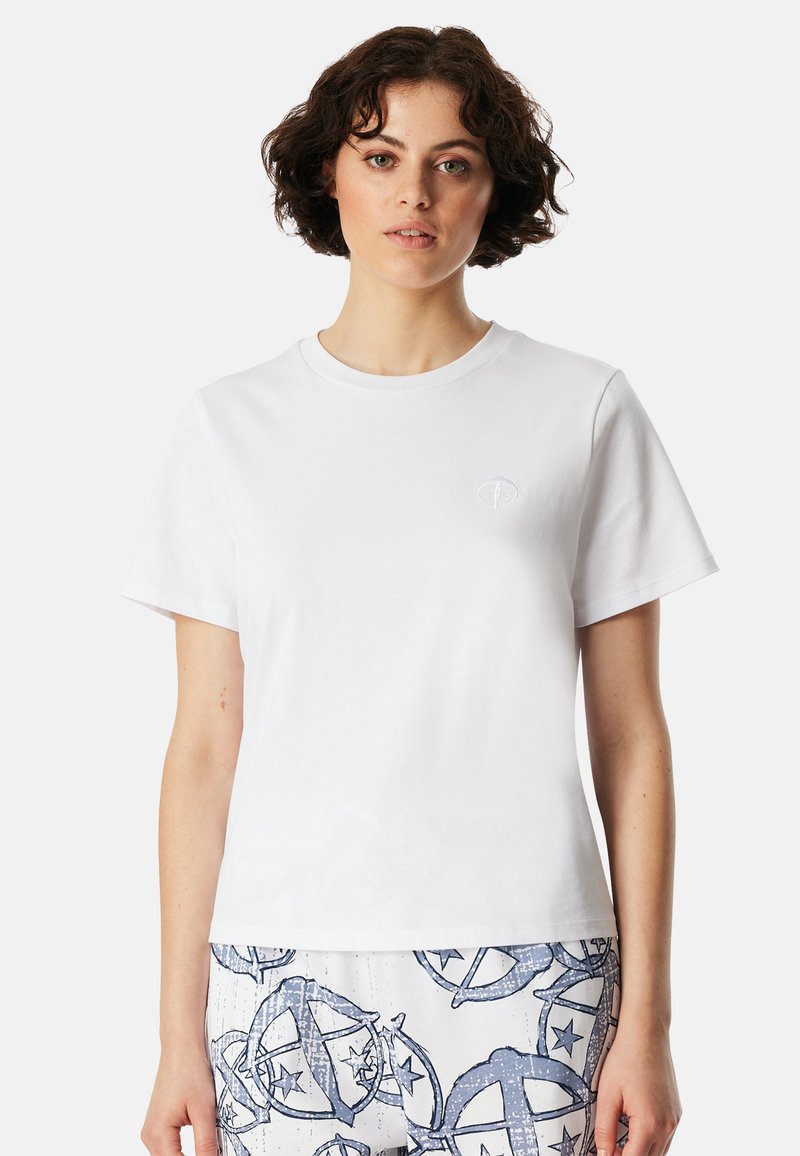 Weißes Baumwoll-T-Shirt mit Rundhalsausschnitt, kurzen Ärmeln und einem kleinen gestickten Logo auf der Brust, kombiniert mit gemusterter Hose.