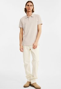 Lichtbeige polo shirt met korte mouwen en een klassieke kraag, gecombineerd met off-white broek en tan instap schoenen.