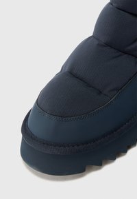 Ciemnoniebieska pufowa boot z teksturowaną cholewką, zaokrąglonym noskiem i grubą gumową podeszwą z zygzakowatym wzorem bieżnika.