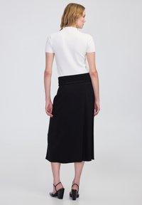 Falda midi negra con cinturilla elástica, combinada con una blusa ajustada de manga corta blanca y sandalias negras de tacón. Textura suave.