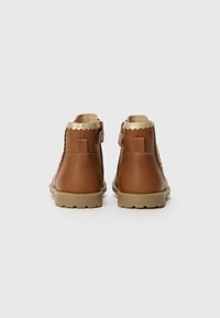 Bottines en cuir marron avec une bordure dorée en forme de vagues sur le dessus, surface texturée et semelle en caoutchouc de couleur claire.