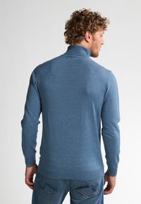 Suéter azul de cuello alto, con puños y dobladillo acanalados; confeccionado en tela de punto con una textura suave. Detalles de costura visibles.