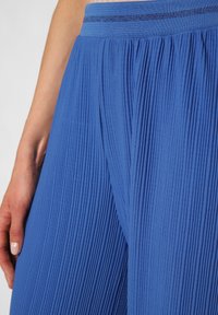 Plissierte blaue Stoffhose mit strukturierten Oberflächen; verfügt über einen weichen Bund mit einem subtilen reflektierenden Streifen; erzeugt glatte Linien und fällt elegant.