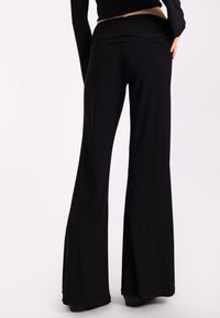 Pantaloni a zampa nera realizzati in tessuto morbido, con una vita ampia e una superficie liscia, caratterizzati da una silhouette lunga e fluente.