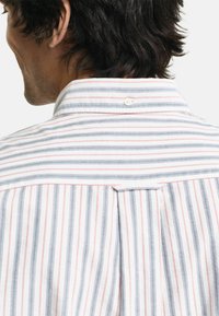 Koszula z długim rękawem w paski z pionowymi niebieskimi, czerwonymi i białymi paskami, z klasycznym kołnierzykiem i szczegółem w postaci pliski na plecach. Teksturowana tkanina.