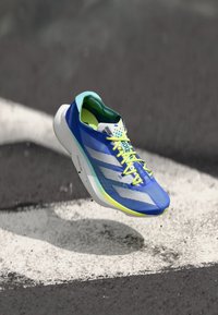 Bottine de sport bleue avec un dessus en maille, des rayures blanches et des lacets jaunes vifs. Design léger avec une semelle épaisse et des motifs texturés.