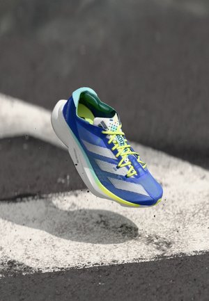 Modrá sportovní bota s síťovaným svrškem, bílými pruhy a jasně žlutými tkaničkami. Lehký design s tlustou podrážkou a texturovanými vzory.