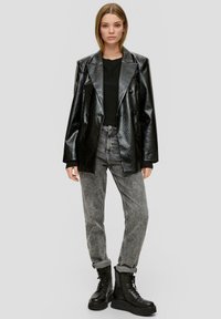 Schwarze, glänzende, doppelt-knöpfte Blazer mit ausgeprägter Textur, kombiniert mit grauen, tapered Jeans und schwarzen, schnürbaren Plateaustiefeln.