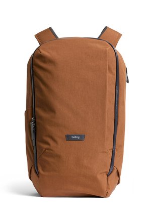 Zaino in tessuto marrone con texture liscia, dotato di una cerniera scura e dettagli in colore scuro, spallacci imbottiti e una toppa con logo frontale.