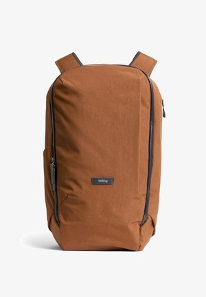 Zaino in tessuto marrone con texture liscia, dotato di una cerniera scura e dettagli in colore scuro, spallacci imbottiti e una toppa con logo frontale.