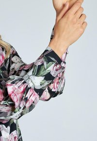 Blusa floreale con base nera; presenta motivi di fiori rosa e bianchi, maniche a sbuffo e dettagli con bottoni ai polsini.