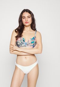 Top de bikini florido com base rosa, apresentando padrões de folhas azuis e verdes; combinado com um fio dental branco texturizado. Tecido suave, alças ajustáveis.