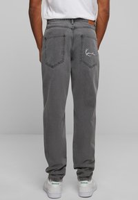 Sive traperice ravnog kroja nogavica, s dva stražnja džepa i bijelim izvezenim detaljem na desnom džepu. Uparene su s bijelim tenisicama.