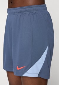 Men's athletic shorts in dark blue fabric with light blue side panel, elastic waistband, and red Nike logo on the left leg.