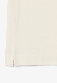 Tissu blanc texturé avec un motif subtil ; présente des fentes latérales à l'ourlet ; design épuré et simple.