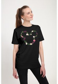 T-shirt noir avec un motif de cœur floral comprenant des fleurs roses et blanches et des feuilles vertes, fabriqué en tissu doux, à manches courtes et coupe décontractée.