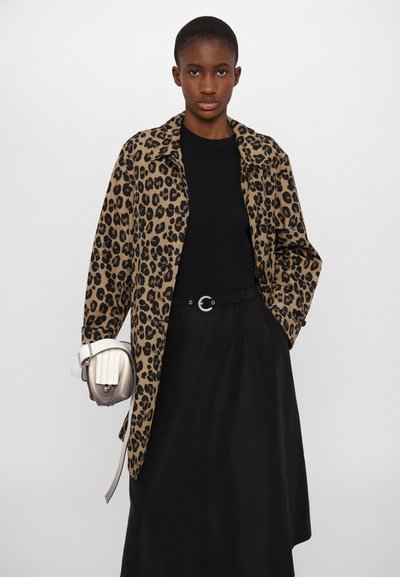 Leopardmönstrad kappa i beige och svart, med krage och lös passform. Bärs över en svart topp med bälte, och håller en liten vit handväska.