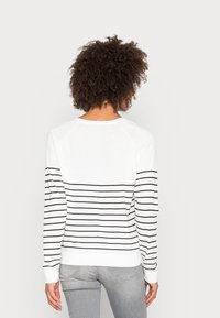 Biała bluza z długim rękawem w czarne poziome paski, z okrągłym dekoltem i ściągaczami na mankietach, wykonana z miękkiej tkaniny z bawełnianej mieszanki.