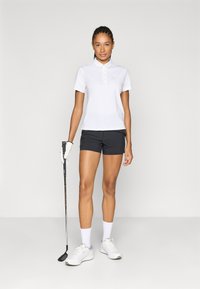 Λευκό πόλο πουκάμισο με κουμπιά, συνδυασμένο με μαύρο σορτς. Κρατάει ένα ρόπαλο γκολφ, φορά γάντι και λευκά αθλητικά παπούτσια με γκρι λεπτομέρειες.