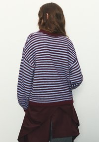 Pruhovaný pletený sveter v bordovej a svetlomodrej farbe, s voľným strihom, spustenými ramenami a rebrovaným lemom, nosený cez bordovú vrstvu.