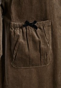 Barna kordbársony anyag, függőleges bordázattal, begyűrt zsebbel és fekete bársony masnival díszítve.