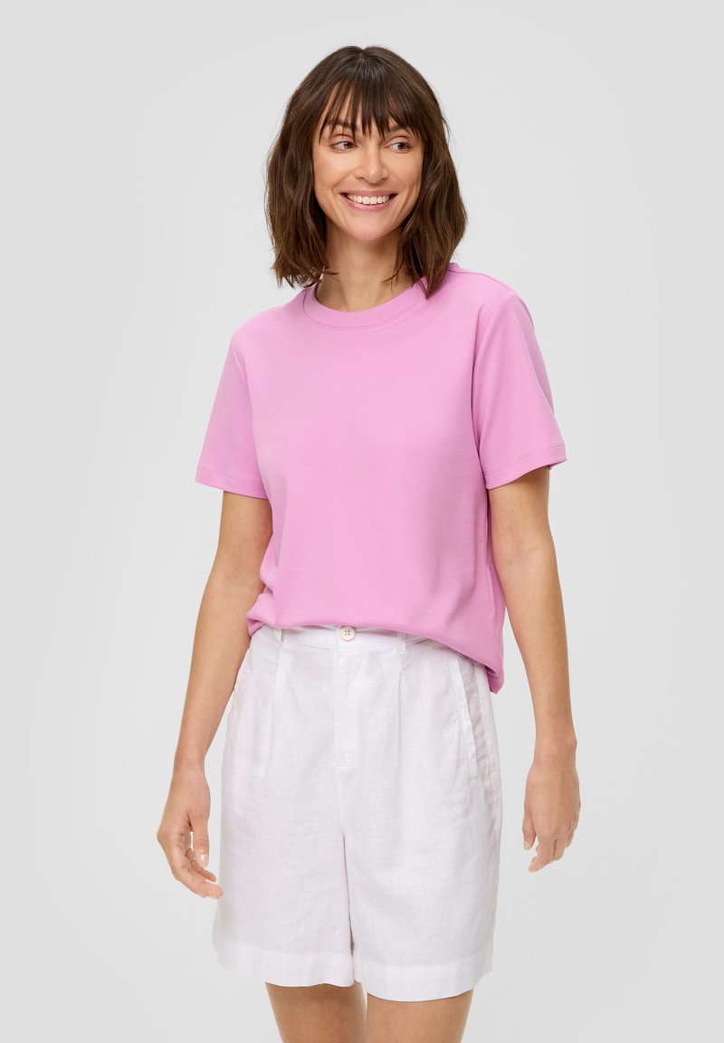 Różowy bawełniany T-shirt z krótkim rękawem, okrągłym dekoltem i luźnym krojem, zestawiony z białymi lnianymi szortami z zapięciem na guzik.
