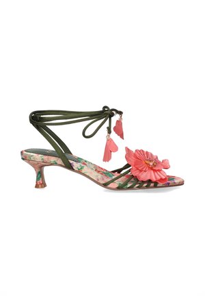 Sandalia verde con tiras, suela con estampado floral, detalle de flor rosa en el dedo y lazos en el tobillo adornados con charms en forma de pétalos rosas.