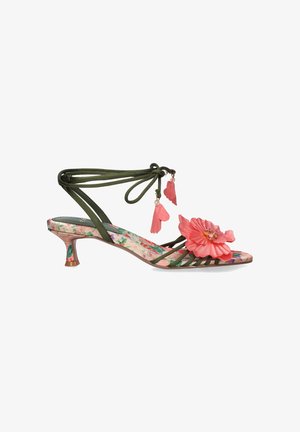 Sandalia verde con tiras, suela con estampado floral, detalle de flor rosa en el dedo y lazos en el tobillo adornados con charms en forma de pétalos rosas.