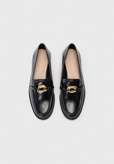 Black leather loafers with a rounded toe, featuring a gold chain accent and stitched details along the sole. Smooth texture throughout.