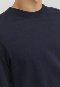 Tumesinane crew-neck särk, mis on valmistatud pehmest puuvillast. Omab soonikust kaelust ja sujuvat, kergelt tekstureeritud pinda.