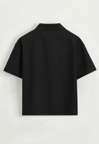 Chemise noire à manches courtes avec un col classique. Texture lisse, silhouette carrée, vue de dos. Pas de motifs ni d'accents visibles.