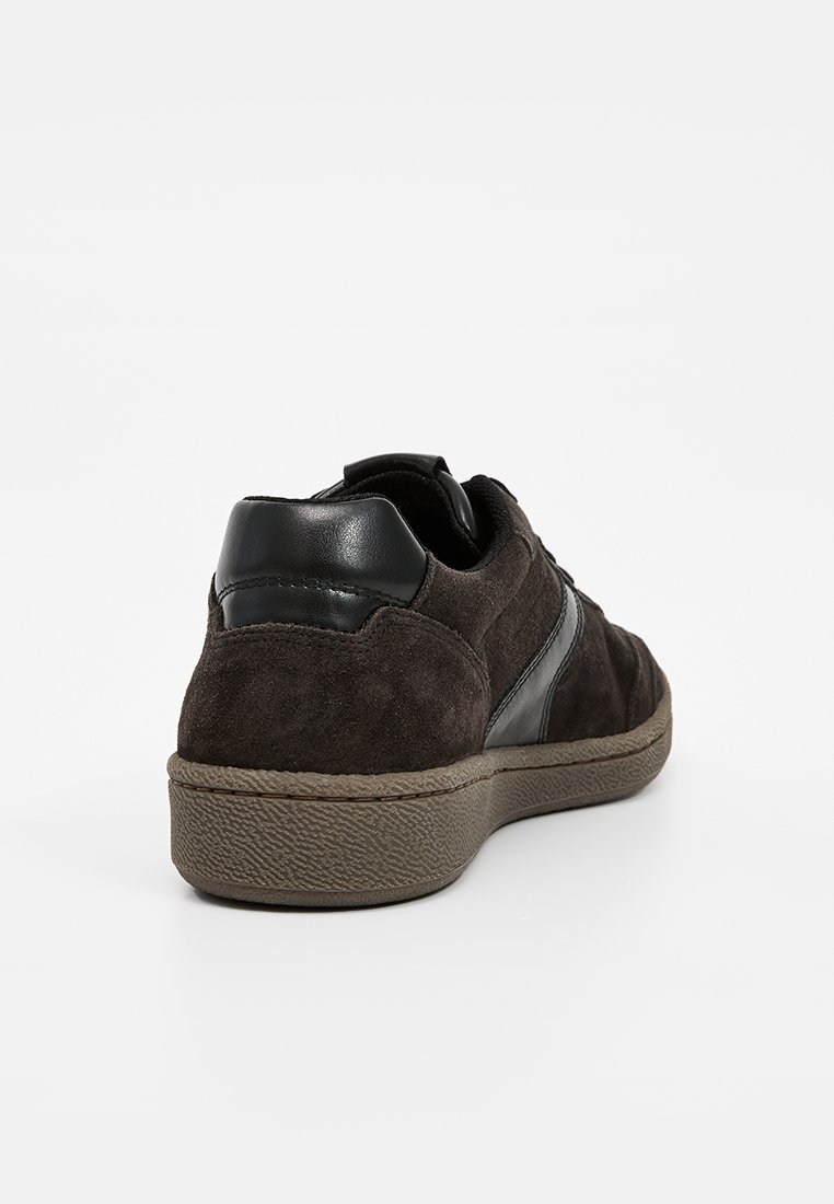 Baskets en daim marron foncé avec des accents en cuir noir, une semelle en caoutchouc texturée et un design à bout rond. Présente des détails de couture minimalistes.