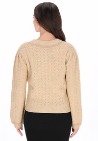 Beżowy sweter wykonany na drutach z fakturowanym wzorem, z prążkowanymi mankietami i dołem oraz okrągłym dekoltem. Posiada bufiaste rękawy dla lepszego efektu objętości.