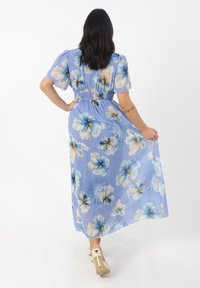 Maxikleid aus hellblauem Chiffon mit floralen Mustern in Weiß und Blau. Elastischer Bund, kurze Puffärmel und bodenlanger Schnitt.
