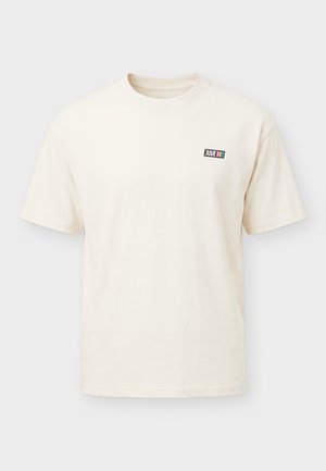 Krémové tričko s krátkym rukávom a okrúhlym výstrihom s malým čiernym obdĺžnikovým logom „JUUE“ a tromi vertikálnymi farebnými pásmi na hrudi.