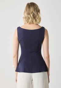 Marinblå peplumtop med en slät, figurnära design, bred halsringning och subtila sömdetaljer. Tillverkad av stretchigt tyg, som visar en skräddarsydd silhuett.