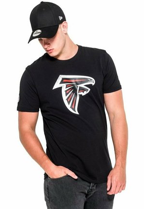 Schwarzes T-Shirt mit einem großen roten und weißen Atlanta Falcons Logo. Der Träger kombiniert es mit einer schwarzen Mütze und dunklen Jeans.
