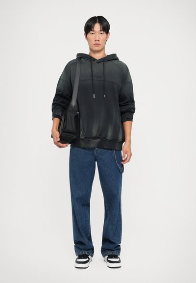 Fekete gradient kapucnis pulóver elülső zsebbel és húzózsinórral, kék farmernadrággal párosítva. Fekete keresztpántos táska, fehér és fekete sportcipők.