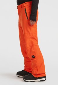 Heldere oranje sneeuwbroeken met een losse pasvorm, gemaakt van weerbestendig materiaal. Voorzien van ritszakken en verstelbare boorden. Zwarte logopatch.