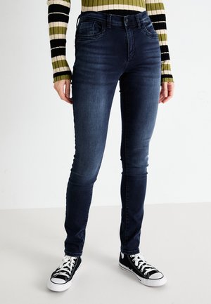 Dark wash, skinny jeans with a smooth texture, featuring front pockets and belt loops, paired with black high-top sneakers.