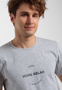 Szary bawełnowy T-shirt z okrągłym nadrukiem graficznym, zawierającym napisy "HOME RELAX" oraz "PAWO SINCE 1989" w ciemnoniebieskim kolorze. Design z okrągłym dekoltem.