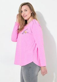 Top a maniche lunghe rosa con grafica a stella; presenta cuciture a contrasto sulle spalle e un orlo hi-lo; realizzato in un tessuto leggero e testurizzato.