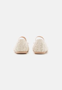 Ballerine in pizzo con un motivo floreale beige, punta rotonda e parte superiore in tessuto morbido. Caratterizzate da una fascia stretta attorno alla caviglia e suola piatta.