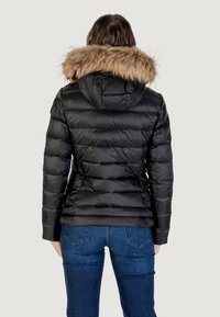 Svart pufferjacka med huva, försedd med en faux fur-kant. Designen inkluderar horisontella quiltade sektioner och en figurnära silhuett.