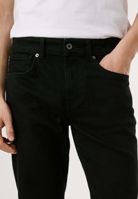 Mustmustest denim püksid otse lõikega, standardse tõmbluku ja nööbiga, ees olevate taskutega ning peene tekstuuriga viimistlusega.