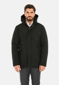 Giacca isolante nera con chiusura a zip, cappuccio e due tasche laterali. Presenta una texture liscia e un design pulito e moderno.