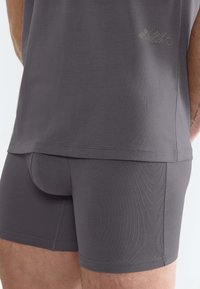 Boxer da uomo in tessuto jersey grigio con una vestibilità aderente, texture liscia e branding sottile sulla vita. Design semplice e senza cuciture.