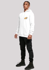 Felpa bianca con tasca frontale e grafica di cartoni colorata, abbinata a pantaloni cargo neri e sneakers nere. Tessuto testurizzato, vestibilità ampia.